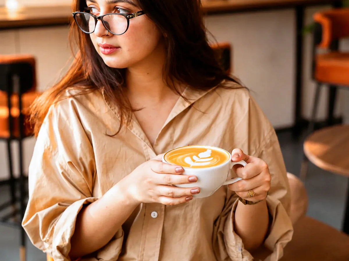 Woman holding a freshly brewed latte with latte art while relaxing in a cozy café.