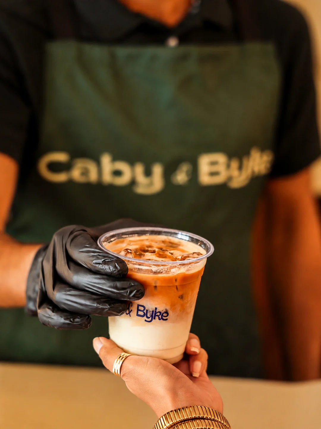 Barista serving a handcrafted iced Spanish latte with rich espresso and creamy milk